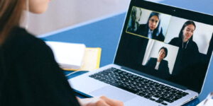 Eine Frau sitzt bei einer Videokonferenz vor ihrem Laptop. Auf dem Bildschirm sind drei GesprÃ¤chspartner zu sehen.