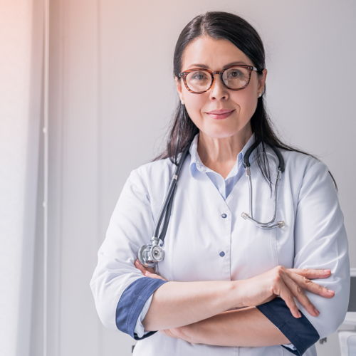 Eine Ärztin mit dunklen Haar und Brille, die ein Stethoskop um den Hals trägt.