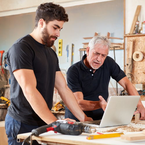 Ein Tischlermeister und sein Geselle in der Werkstatt mit einem Laptop zur Überprüfung des Datenschutz in ihrem Handwerk.