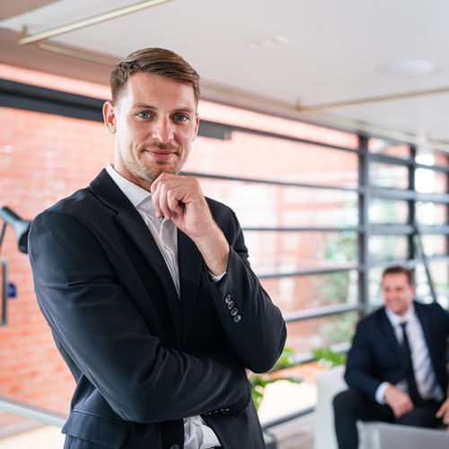 Ein junger Mann im dunklen Anzug in steht in einem sehr hellen Büro.